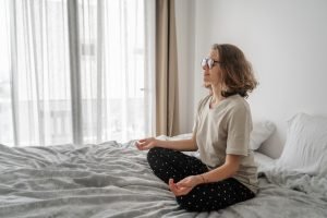 Beautiful young curly woman in glasses sits on a bed in a lotus